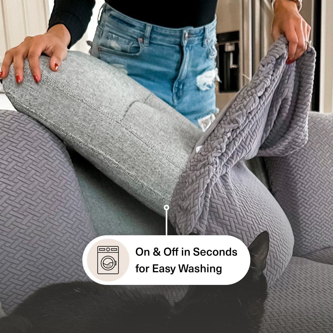 Woman pulling a grey Magic Sofa Cover Classic onto a back cushion while a black cat lies on the sofa