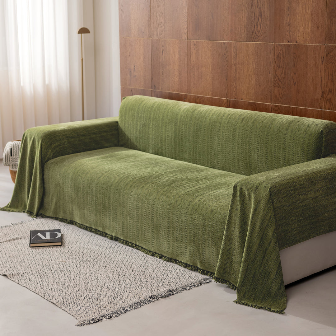 Angled view of a sofa covered in the Kale Lena Herring Magic Sofa Blanket, fringed edge visible