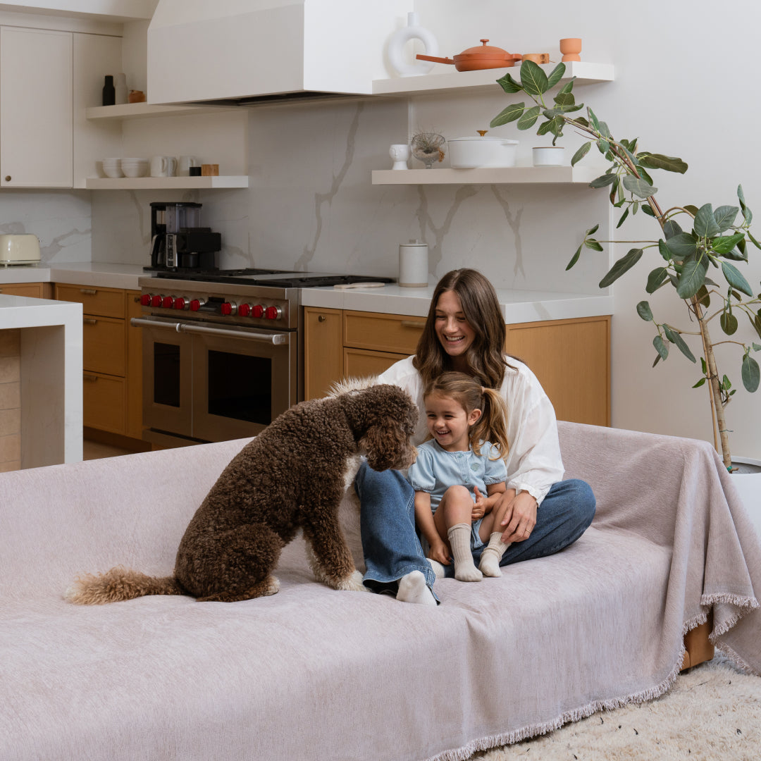 Woman and girl on a sofa covered in the Cookie Sophie Plush Magic Sofa Blanket, facing a dog