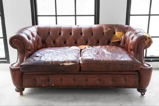 Worn brown leather Chesterfield sofa with cracked, peeling seat cushions