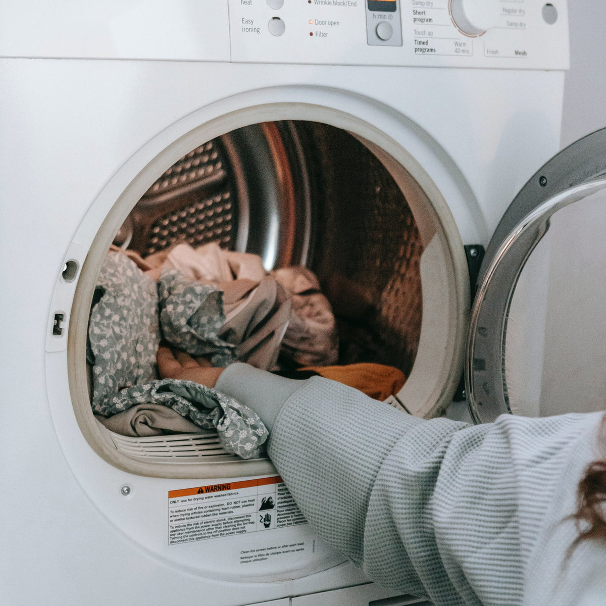 Person loading fabric covers into an open front-loading tumble dryer