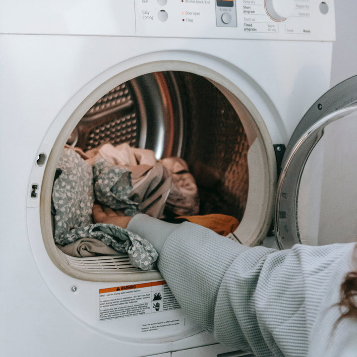 Person loading fabric covers into an open front-loading tumble dryer