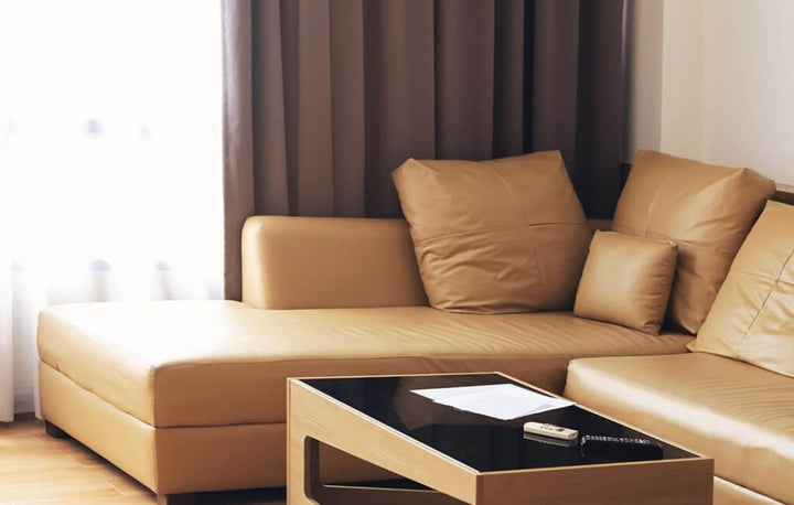 Tan leather chaise sectional with matching cushions and a glass-top coffee table in a living room