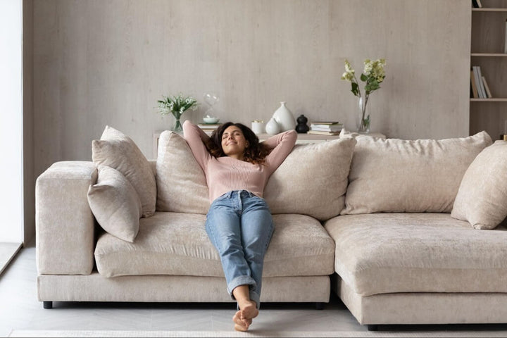 Woman relaxing on a cream chaise sectional with plush cushions in a bright living room