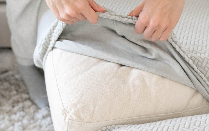 Hands fitting a grey textured stretch cover over a beige sofa cushion