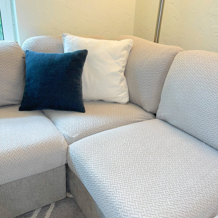 Corner sectional with light grey textured stretch cushion covers, a navy pillow and a white pillow