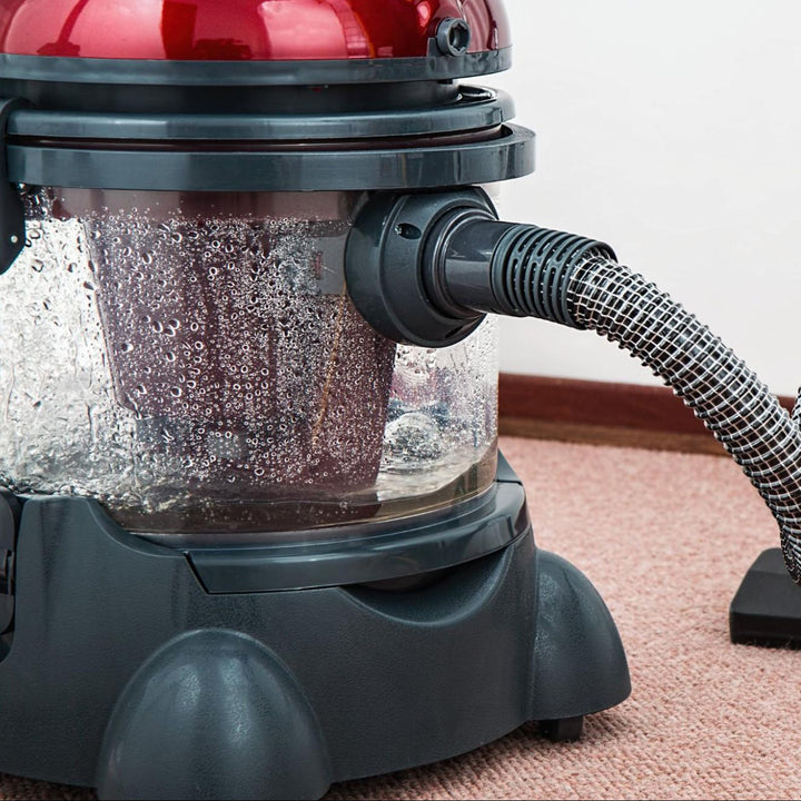 Red canister vacuum cleaner with a water tank and hose on a pink carpet