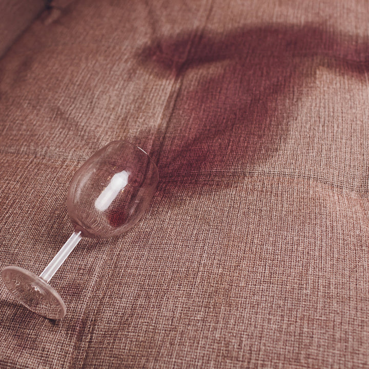 Tipped-over wine glass beside a red wine stain on a brown fabric couch