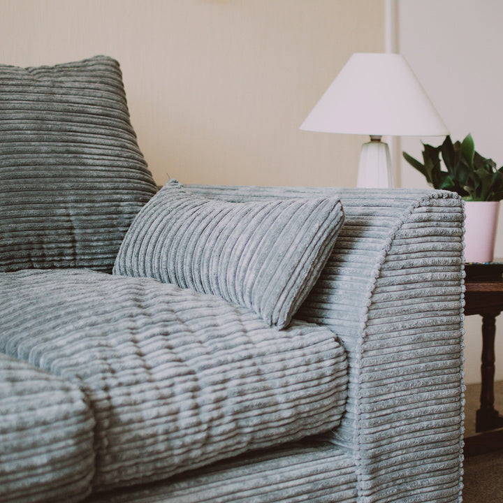 Grey jumbo cord sofa with plush cushions and a bolster pillow beside a lamp and potted plant