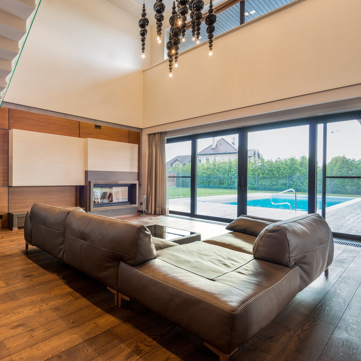Brown leather sectional sofa in a double-height living room with glass doors opening onto a pool