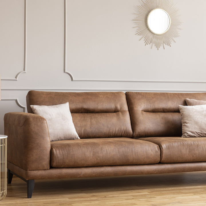 Brown leather sofa with beige throw pillows under a gold sunburst mirror