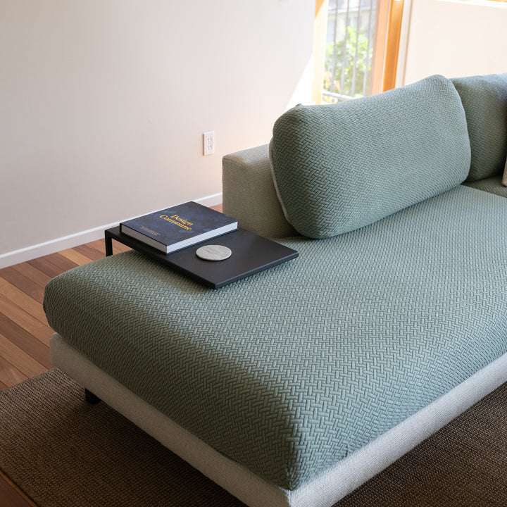 Chaise sectional with sage green textured stretch cushion covers and a black side tray holding a book