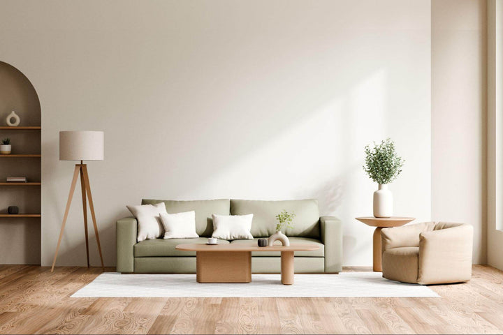 Sage green sofa with white cushions in a minimalist living room with a wooden coffee table and floor lamp
