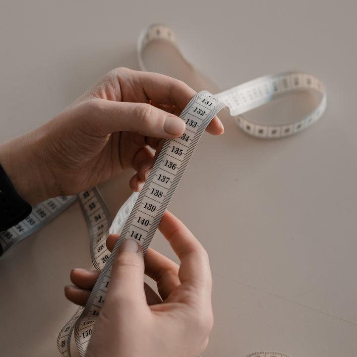 Hands holding a white measuring tape over a table