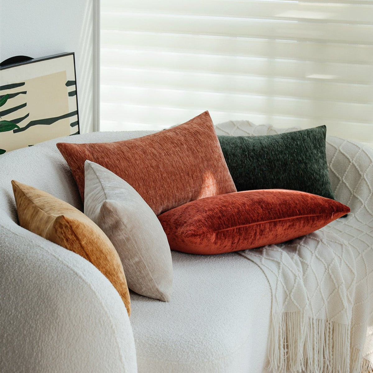 Woody pillow covers in rust, green, gold and beige on a curved white boucle sofa with a knit throw
