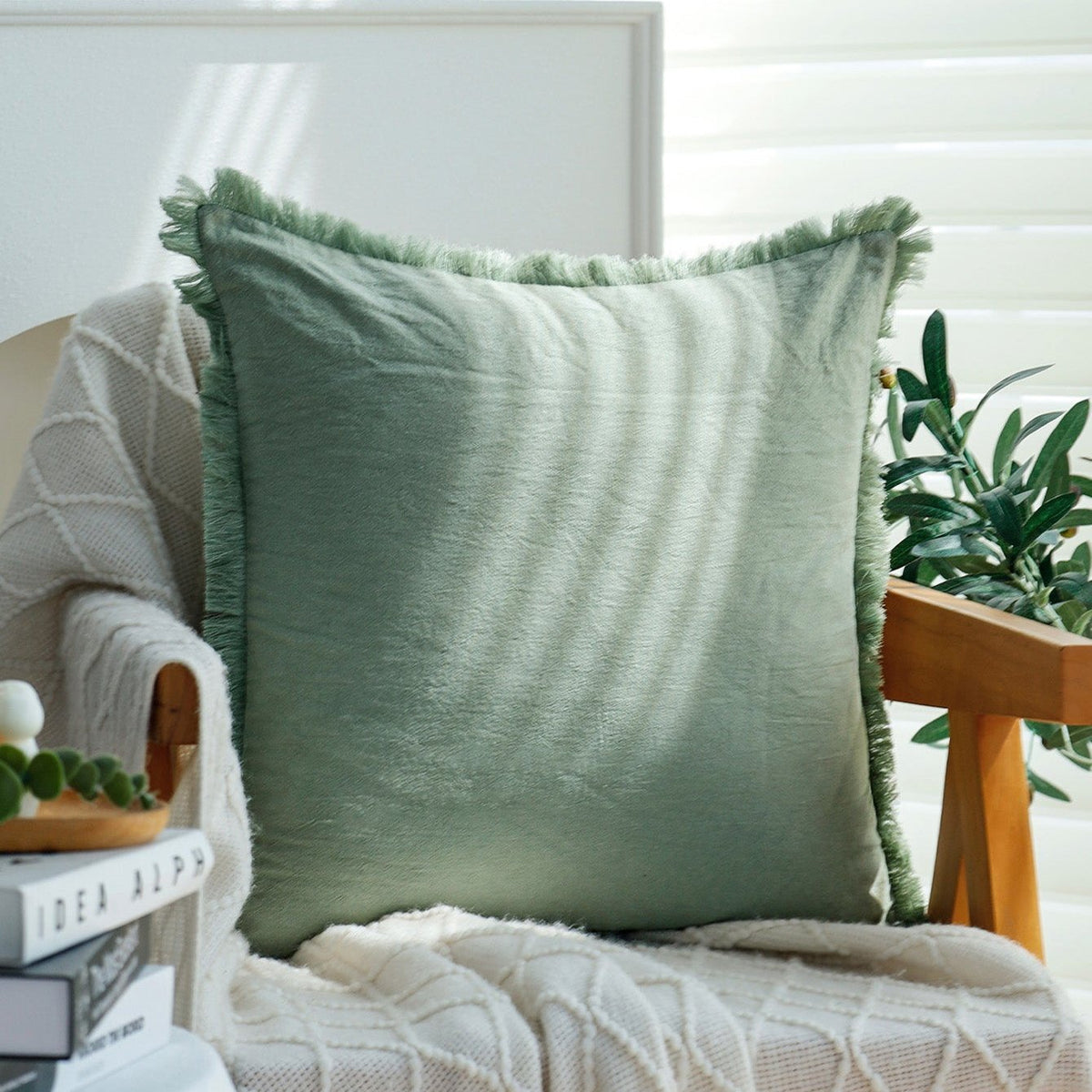 Fringe pillow cover in Sage on a wooden armchair with a cream knit throw