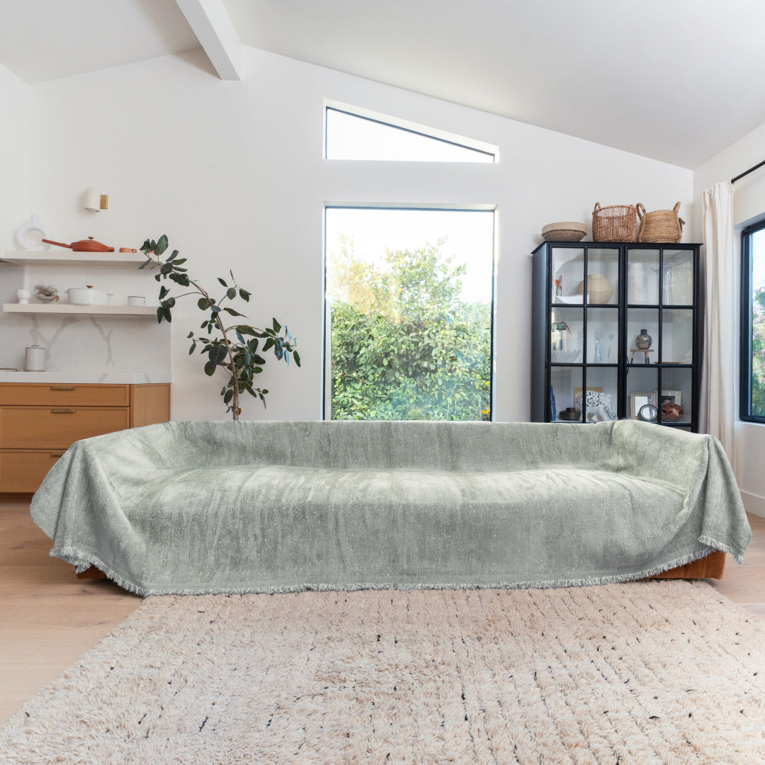Kale Iris Sprinkle Magic Sofa Blanket draped over a long sofa in a living room with large windows