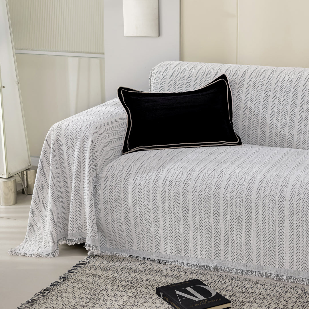Angled view of a sofa covered in the Caviar Lena Herring Magic Sofa Blanket, fringed edge visible