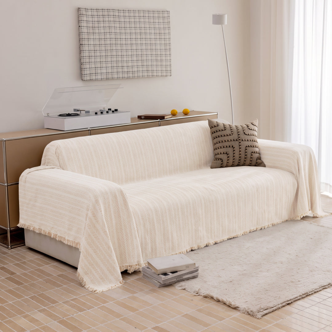 Angled view of a sofa covered in the Latte Lena Herring Magic Sofa Blanket, fringed edge visible