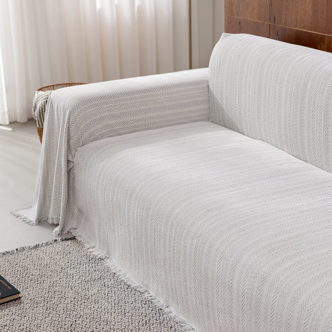 Angled view of a sofa covered in the Sesame Lena Herring Magic Sofa Blanket, fringed edge visible