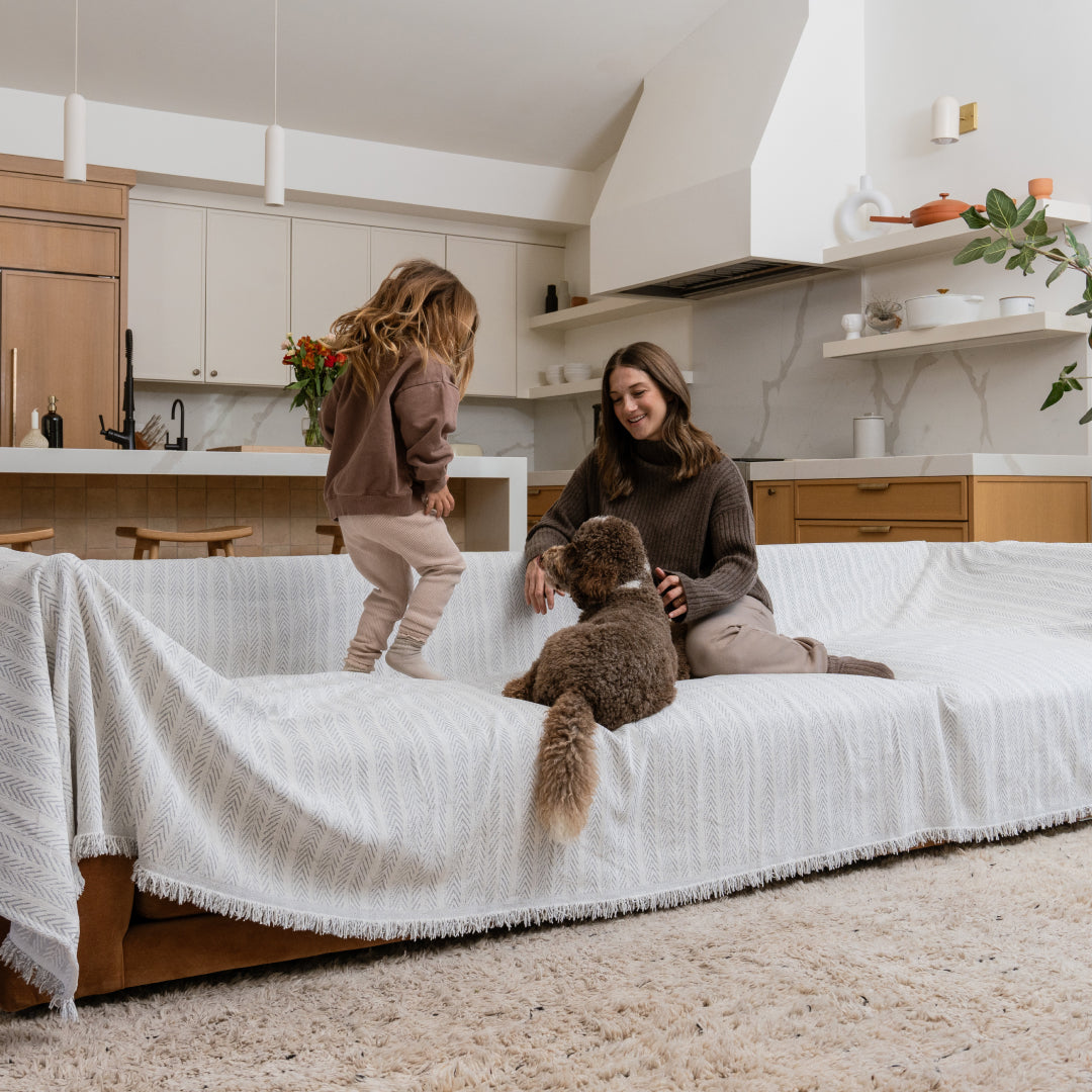 Woman, girl and curly-coated dog on a sofa covered in the Sesame Lena Herring Magic Sofa Blanket