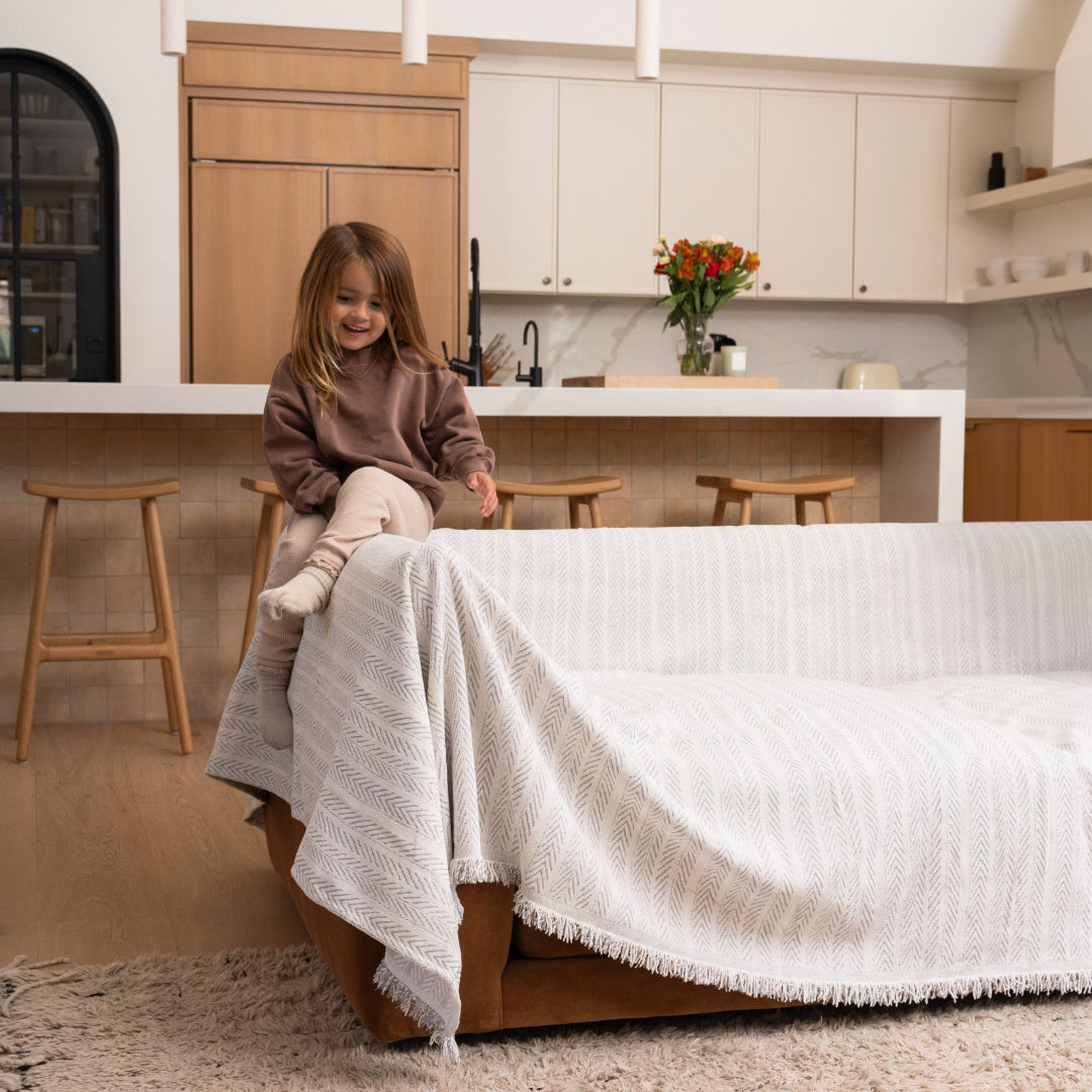 Girl sitting on the arm of a sofa covered in the Sesame Lena Herring Magic Sofa Blanket