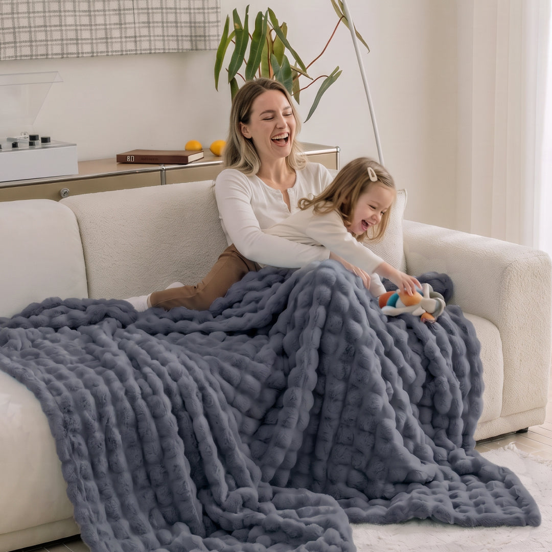 Person lounging on a sofa covered in the Black Sesame Nora Mink Magic Sofa Blanket