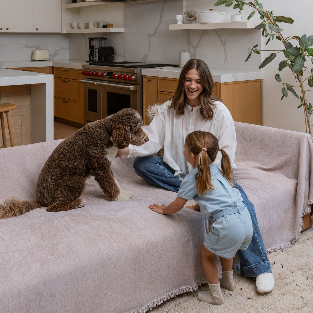 Woman, girl and curly-coated dog on a sofa covered in the Cookie Sophie Plush Magic Sofa Blanket